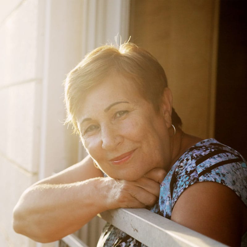 a woman with short hair and a patterned shirt leaning out the window of a certified community behavioral health clinic with the sun shining down